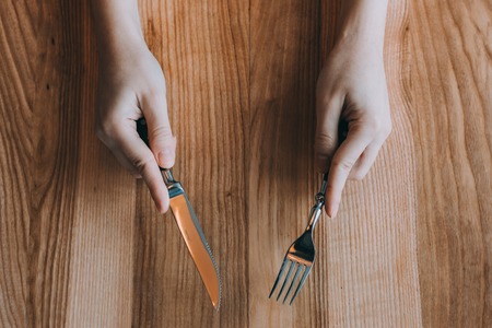 Hand holding fork and knife on wooden background, flatlay composition. food colectionの写真素材
