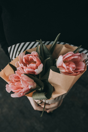 Woman hand holding soft pink tulips flowers bouquet decorated with kraft paper. blurred backgrpundの写真素材