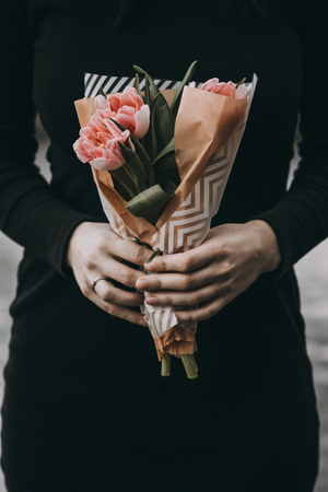 Woman hand holding soft pink tulips flowers bouquet decorated with kraft paper. blurred backgrpundの写真素材