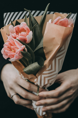 Woman hand holding soft pink tulips flowers bouquet decorated with kraft paper. blurred backgrpundの写真素材