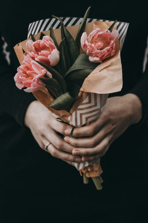 Woman hand holding soft pink tulips flowers bouquet decorated with kraft paper. blurred backgrpundの写真素材