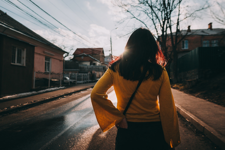 woman standing alone on street in the sun light. back view. Illuminationの写真素材