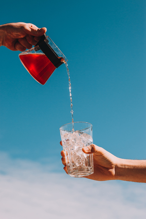 Freash rose lemonade pouring in a glass with ice with cloud sky background. Summer drinks conceptの写真素材