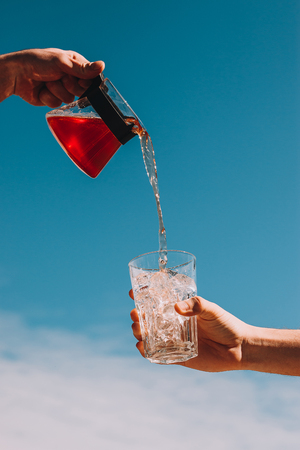 Freash rose lemonade pouring in a glass with ice with cloud sky background. Summer drinks conceptの写真素材