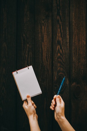 Female hands holding note and pen on a wooden background. Student