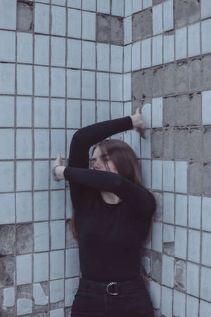 the girl driven into a corner in fear stands and looks and twists her handsの写真素材