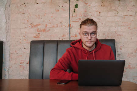 Portrait of happy male freelancer in optical eyewear for vision correction smiling at camera during break from web working online, cheerful hipster blogger sitting in cafe with mockup laptopの写真素材