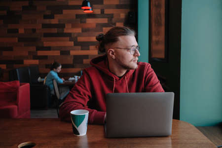 Portrait of happy male freelancer in optical eyewear for vision correction smiling at camera during break from web working online, cheerful hipster blogger sitting in cafe with mockup laptopの写真素材