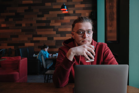 Portrait of happy male freelancer in optical eyewear for vision correction smiling at camera during break from web working online, cheerful hipster blogger sitting in cafe with mockup laptopの写真素材