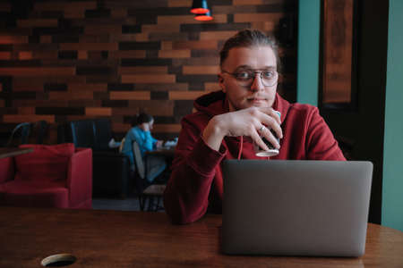 Portrait of happy male freelancer in optical eyewear for vision correction smiling at camera during break from web working online, cheerful hipster blogger sitting in cafe with mockup laptopの写真素材