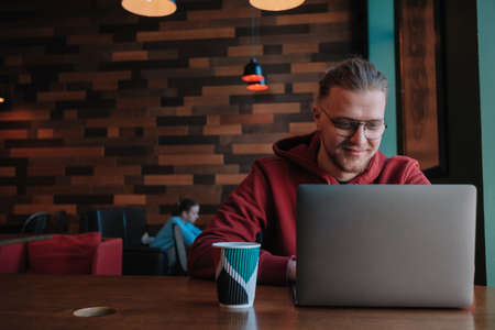 Portrait of happy male freelancer in optical eyewear for vision correction smiling at camera during break from web working online, cheerful hipster blogger sitting in cafe with mockup laptopの写真素材