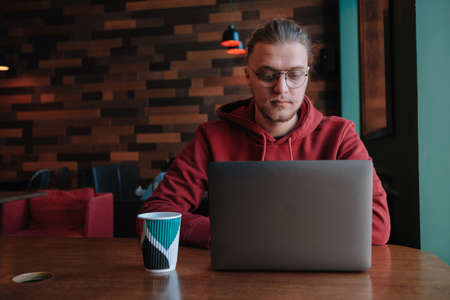 Portrait of happy male freelancer in optical eyewear for vision correction smiling at camera during break from web working online, cheerful hipster blogger sitting in cafe with mockup laptopの写真素材