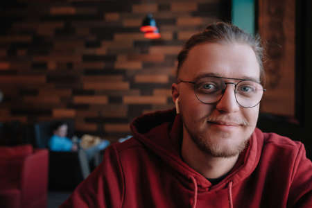 Portrait of happy male freelancer in optical eyewear for vision correction smiling at camera during break from web working online, cheerful hipster blogger sitting in cafe with mockup laptopの写真素材