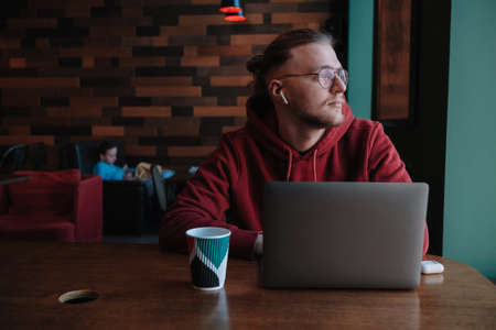 Portrait of happy male freelancer in optical eyewear for vision correction smiling at camera during break from web working online, cheerful hipster blogger sitting in cafe with mockup laptopの写真素材