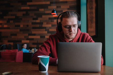 Portrait of happy male freelancer in optical eyewear for vision correction smiling at camera during break from web working online, cheerful hipster blogger sitting in cafe with mockup laptopの写真素材