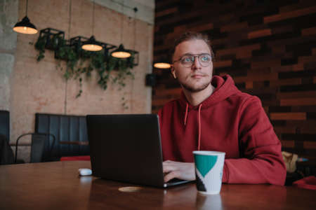 Portrait of happy male freelancer in optical eyewear for vision correction smiling at camera during break from web working online, cheerful hipster blogger sitting in cafe with mockup laptopの写真素材
