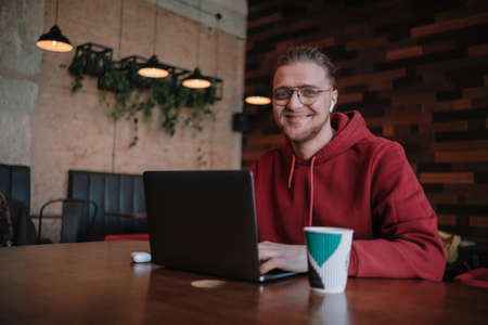Portrait of happy male freelancer in optical eyewear for vision correction smiling at camera during break from web working online, cheerful hipster blogger sitting in cafe with mockup laptopの写真素材