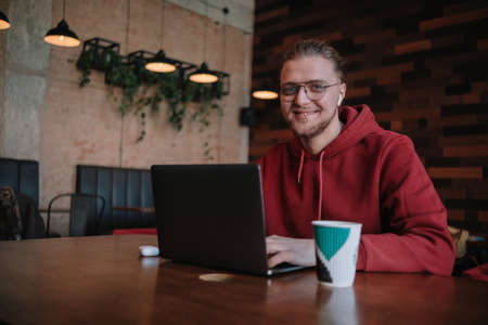 Portrait of happy male freelancer in optical eyewear for vision correction smiling at camera during break from web working online, cheerful hipster blogger sitting in cafe with mockup laptopの写真素材