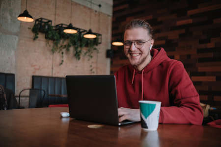Portrait of happy male freelancer in optical eyewear for vision correction smiling at camera during break from web working online, cheerful hipster blogger sitting in cafe with mockup laptopの写真素材