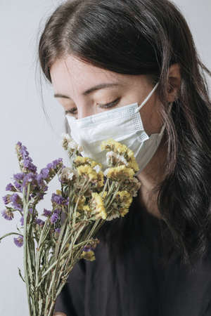 Young woman in protective medical mask sniffing yellow flowerの写真素材