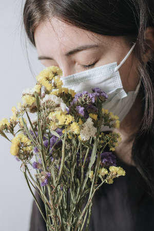 Young woman in protective medical mask sniffing yellow flowerの写真素材