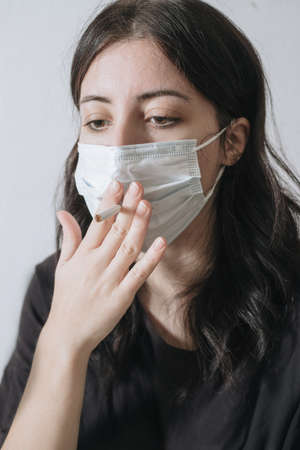 Senior woman hold a cigarette in mouth,withdrawal symptoms,cigarette cravings,feeling stressful while wear a face mask during the pandemic virus,elderly female is addictedの写真素材