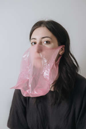 Pandemic self isolation. Defocused art portrait. anxiety. Scared woman in protective face mask cellophane bag in red blue neon light on wrinkled polyethyleneの写真素材