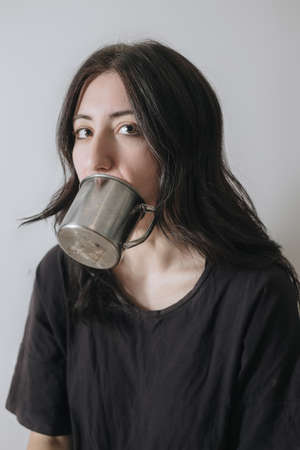 Young woman with a cup of tea at the window during quarantine wearing face mask worried about the new lifestyle.の写真素材