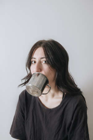 Young woman with a cup of tea at the window during quarantine wearing face mask worried about the new lifestyle.の写真素材