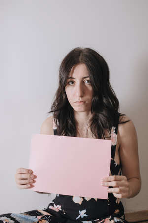 Sad young woman holding a blank banner. Woman holding blank sheet of paperの写真素材