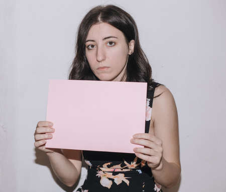 Sad young woman holding a blank banner. Woman holding blank sheet of paperの写真素材