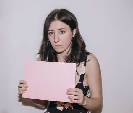 Sad young woman holding a blank banner. Woman holding blank sheet of paperの写真素材