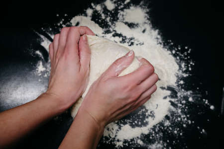 Pizza dough on a black table with handsの写真素材