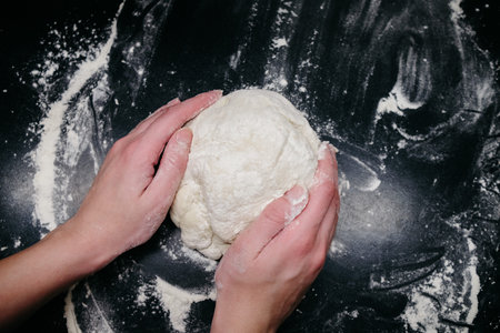 Pizza dough on a black table with handsの写真素材