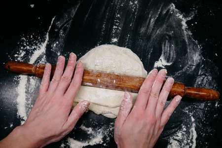 Pizza dough on a black table with handsの写真素材