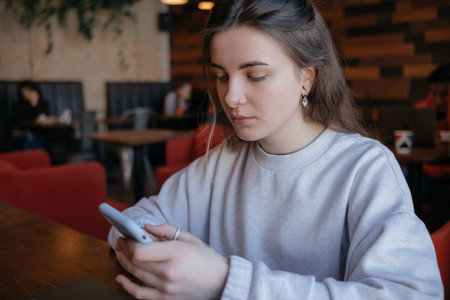 Happy smiling gorgeous woman in fashionable glasses reading pleasant text message on mobile phone while sitting in coffee shop during recreation time.の写真素材