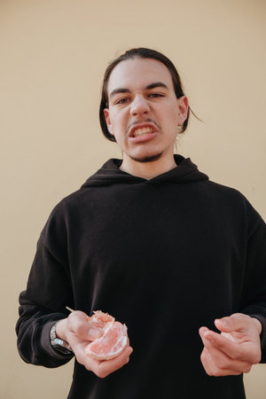 young Caucasian guy bites sour unripe citrus. A man makes a face because of the sour taste of fruit, posing on a green background. Vitamin C.の写真素材