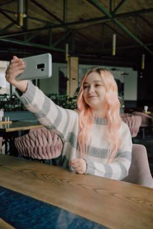 Young woman sitting in a cozy coffehouse drinking coffee and using smartphone.の写真素材