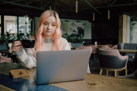 Pretty female student with cute smile keyboarding something on net-book while relaxing after...