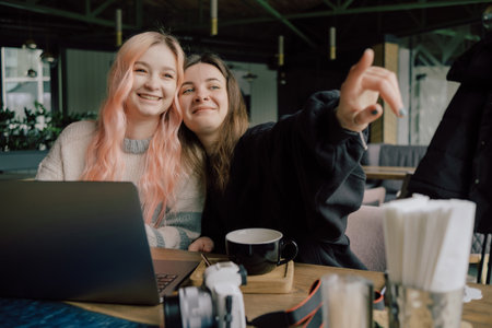 two happy young women sitting in coffee shop looking at laptop computerの写真素材