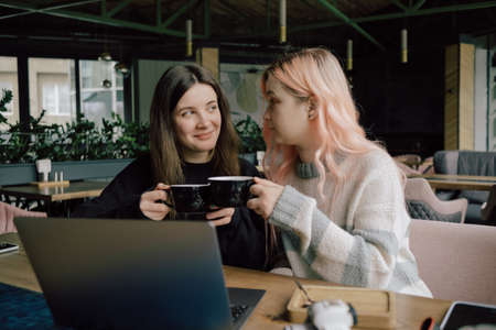 two happy young women sitting in coffee shop looking at laptop computerの写真素材