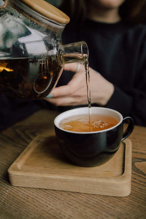 Young woman in cafe during quarantine. Girl pouring some tea from teapot into white cup. Beautiful woman in green sweater smile.の写真素材