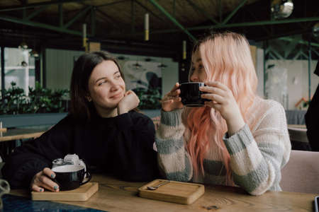 Interracial lesbian couple each other with shy smile, holding hands during lunch at restaurant.の写真素材