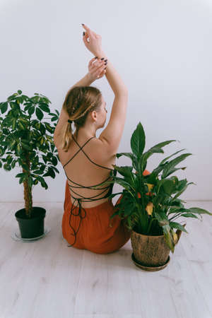 Portrait of young caucasian woman in red cloth sitting near flowerpot rear viewの写真素材