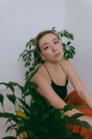 Portrait of young caucasian woman in red cloth sitting near flowerpotの写真素材