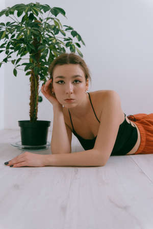 Portrait of young caucasian woman in red cloth laying near flowerpotの写真素材