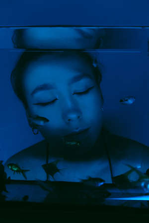 porrait of woman underwater with fish concept blue lightの写真素材