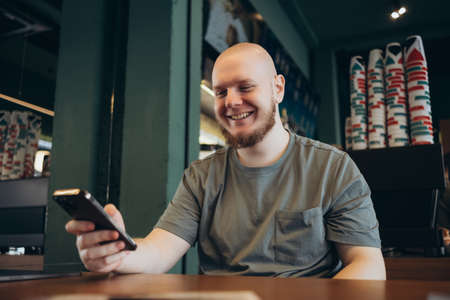 Smartphone man sms texting drinking at cafe summer. Happy casual urban bald bearded manの写真素材