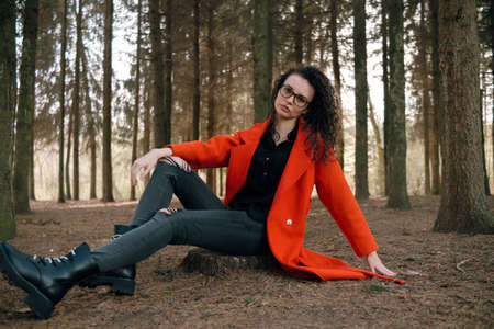 portrait of curly brunette woman in red coat in the parkの写真素材