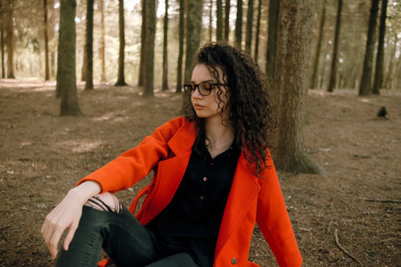 portrait of curly brunette woman in red coat in the parkの写真素材